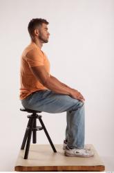 Sitting pose orange thsirt light blue jeans of bodybuilder Harold